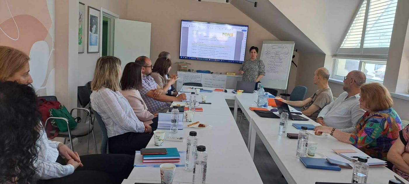 Sesiune de lucru FONSS: participanți la mese dispuse în careu, o vorbitoare prezentând lângă un flipchart.